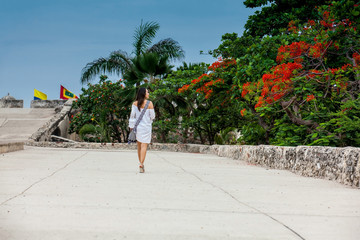 Fototapeta na wymiar Beautiful woman on white dress walking alone at the walls surrounding the colonial city of Cartagena de Indias
