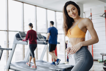 Fototapeta na wymiar young attractive girl in the gym drinking water on the background of treadmills