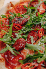 Neapolitan spicy pizza with ham, cheese, arugula, basil, tomatoes, pepperoni pepper sprayed with cheese on a wooden board on a tablecloth in a cell with a place for text