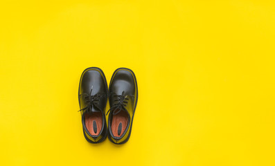 Black leather shoes yellow background top view