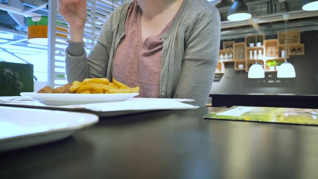 Woman inside food restaurant eating French fries and Swedish meatballs pouring organic potatoes in delicious sauces