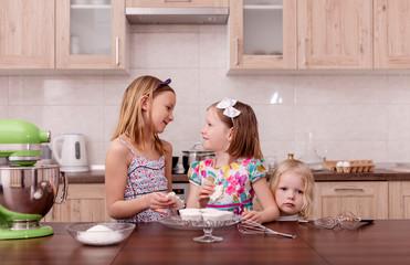 Large family - a mother and three children - two daughters and a son, cook in the kitchen, whip the cream in a blender.