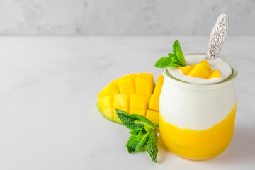 fruit mango yogurt with fresh mint in a glass with a spoon over concrete background. healthy...