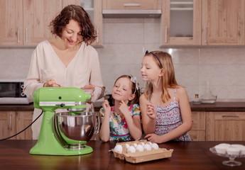 Large family - a mother and three children - two daughters and a son, cook in the kitchen, whip the cream in a blender.