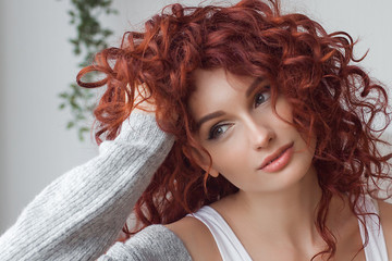 Closeup portrait of young beautiful redhaired woman. Redhead female indoors. Beauty portrait of attractive lady at home with free space.