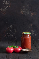 Jar with homemade tomato juice, fresh tomatoes, parsley and salt on a dark wooden background.