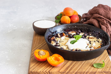 Crumble in cast iron pan with blackcurrant and apricot served with natural yogurt and min. Healthy food concept. 