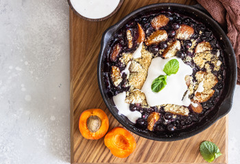 Crumble in cast iron pan with blackcurrant and apricot served with natural yogurt and min. Healthy food concept. 