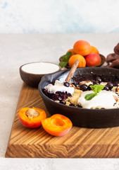 Crumble in cast iron pan with blackcurrant and apricot served with natural yogurt and min. Healthy food concept. 