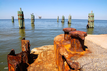 pier with rusty metal poles, in the background an oil drilling platform