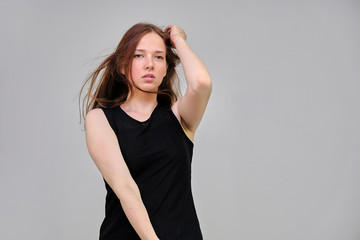 Photo portrait of a beautiful young pretty girl with dark red hair on a gray background in a black jacket. It stands directly in front of the camera in various poses, smiling, happy with life.