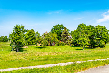 You see a landscape in Lower Saxony with green meadows. Almost hidden from trees stands a typical house for this region.