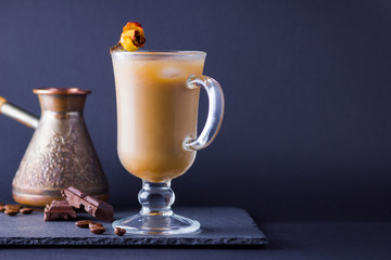 Copper coffee pot (Cezve) and coffee beans. Coffee with milk on dark background. Latte and black chocolate on slate board. Milk drink in glass beaker and dried rose