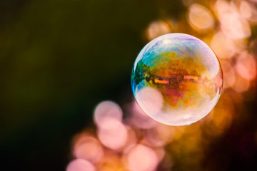 colourful soap bubble floating against a mainly dark background with a streak of light bubble bokeh. There are building reflections in the bubble