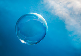 Soap bubble floating in a blue sky with clouds catching the sunlight on its edge.