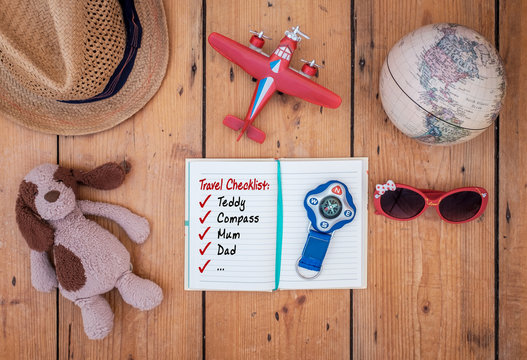Child’s diary and travel accessories laid out on old wooden table. A travel checklist is readable. Travel concept