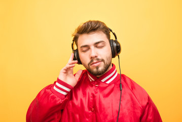 Close-up portrait of an adult man listens to music in headphones with closed eyes on a yellow background. Music enthusiast enjoys music. Isolated