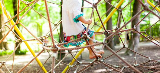 Junges Mädchen klettert im Spinnennetz auf Spielplatz. Children summer activities.