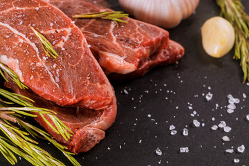 Raw striploin steak with rosemary and garlic, salt and pepper over stone table.