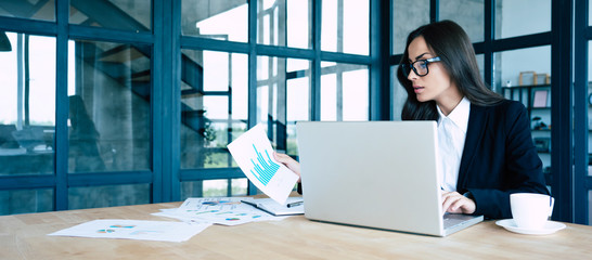 Successful confident beautiful young brunette businesswoman sitting at modern workplace and working...