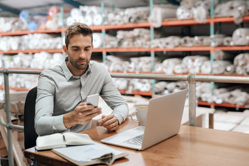 Warehouse manager checking his cellphone while working in his office