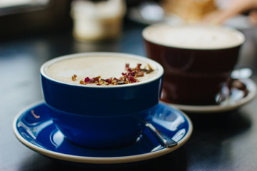Two cups of cappuccino with latte art on black background. Beautiful foam, blue and brown ceramic cups, stylish toning, place for design and text.