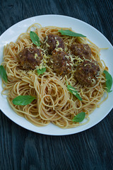 Pasta with meatballs and parsley in tomato sauce. Dark wooden background. View from above.