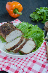 Baked boiled pork in spices sliced on a white plate with green salad. Dark wooden background.