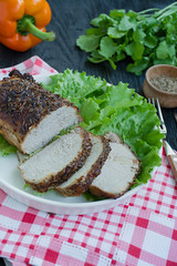Baked boiled pork in spices sliced on a white plate with green salad. Dark wooden background.