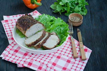 Baked pork tenderloin in spices sliced on a white plate with green salad. Dark wooden background.