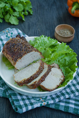 Fototapeta na wymiar Baked pork tenderloin in spices sliced on a white plate with green salad. Dark wooden background.