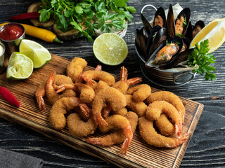 fried breaded shrimps, mussels served with lime on wooden board, delicious deep, red, white sauce