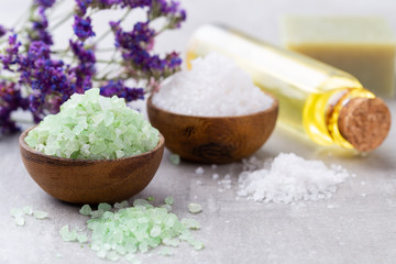 Sea salt in bowl, aroma oil in bottles, Wellness and flowers on grey textured background and flowers on vintage wooden background. Selective focus.