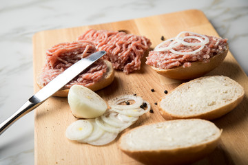 Deutsche Mettbrötchen mit rohen Schweine Mett, Brötchen, Butter, Zwiebeln, Pfeffer und Mett auf Holzbrett mit Messer in Küche