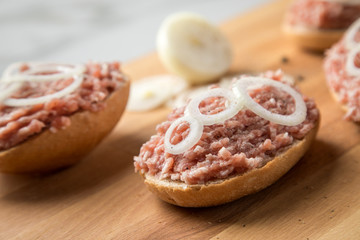 Deutsche Mettbrötchen mit rohen Schweine Mett, Brötchen, Butter, Zwiebeln, Pfeffer und Mett auf Holzbrett mit Messer in Küche