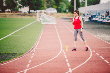 Sports fitness Caucasian women doing warm-up before exercise. Athlete stretching legs doing warm-up before training. Jogging in the city at the stadium. Girl uses headphones handset phone sportswear