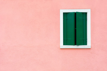 Window with green shutters on the pink wall. Colorful architecture in Burano island, Venice, Italy.