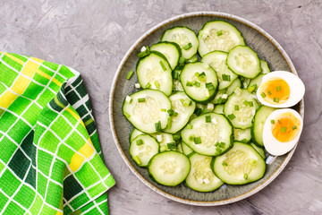 Ready-to-eat fresh cucumber salad, boiled chicken egg and green onions on a plate on the table. Top view