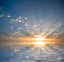 The sun's rays make their way through the clouds at sunset, painting them against the backdrop of the ocean.