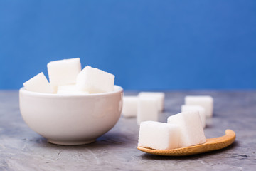 Sugar-free sugar cubes in a white bowl and in a wooden spoon on a table against a blue background