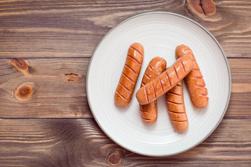 Grilled chicken sausages ready to eat on a plate on a wooden table. Top view. Copy space