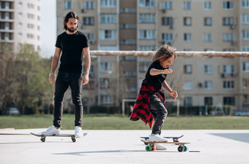 Young father and his son dressed in the stylish casual clothes rides skateboards on a platform...
