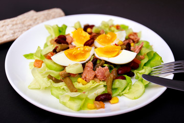 Tuna salad with lettuce, eggs and tomatoes with breads on black table. Diet menu. Top view. Restaurant salad menu concept. Food bloggers background.