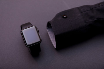 Black shirt with smart watch without hand on grey background.