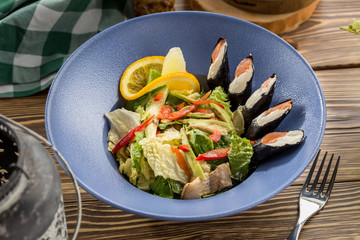 Fresh green salad with salmon cream cheese sushi on the side on wooden table