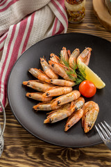 Cooked prawn in shell with lemon on brown plate on wooden table