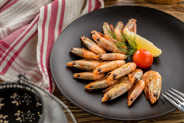 Cooked prawn in shell with lemon on brown plate on wooden table