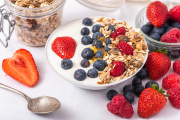 White yogurt in bowl with oatmeal and strawberries, blueberries and raspberries on the top on white background.