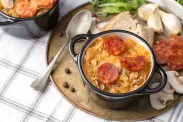 Slovak Christmas national cabbage soup in small black pot with sausage on the tablecloth background.