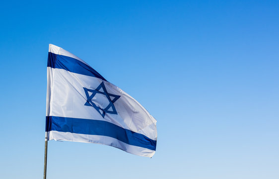 Israeli flag evolving on a wind on empty blue sky background 